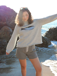 Woman wearing a sweater with a fish design on a rocky beach