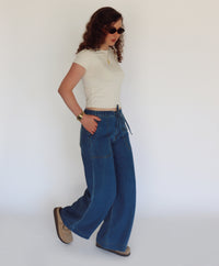 A woman modeling a cream short-sleeve crop top and wide-leg blue jeans against a plain white studio background.