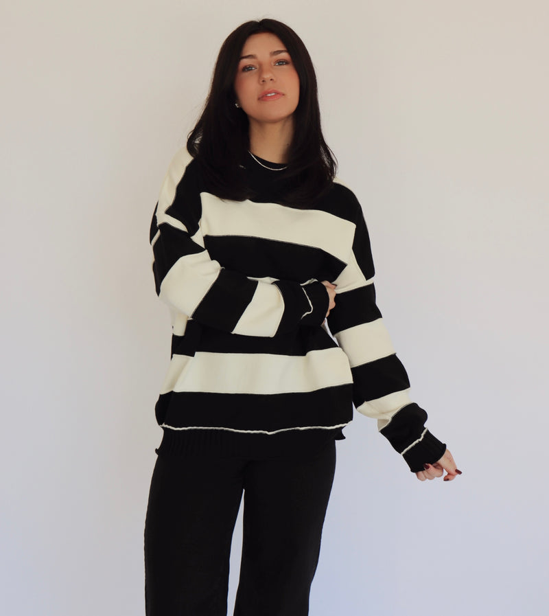 Person wearing a black and white striped pullover and black jeans against a plain background
