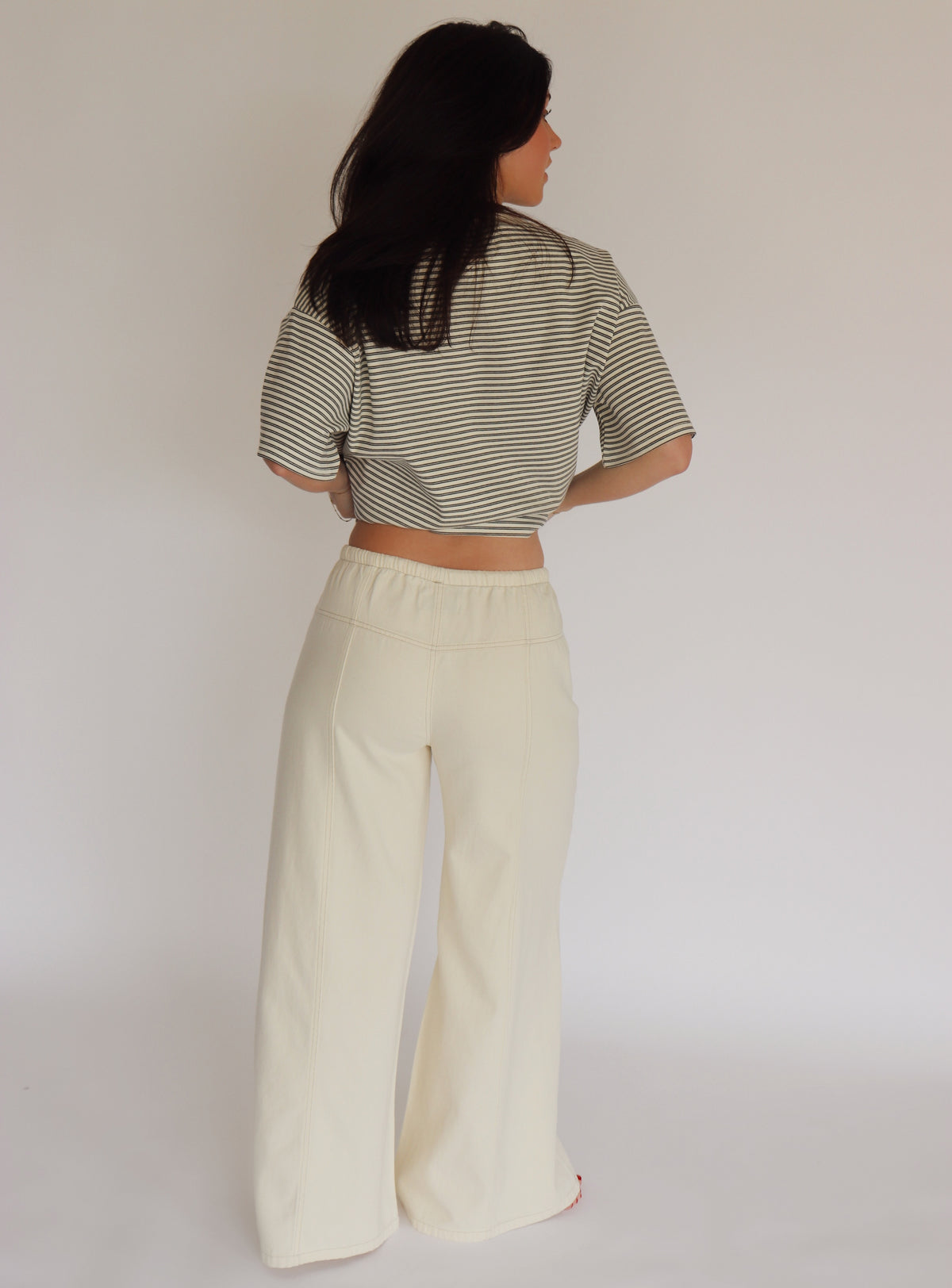 Woman wearing a striped shirt and cream wide-leg pants against a plain background