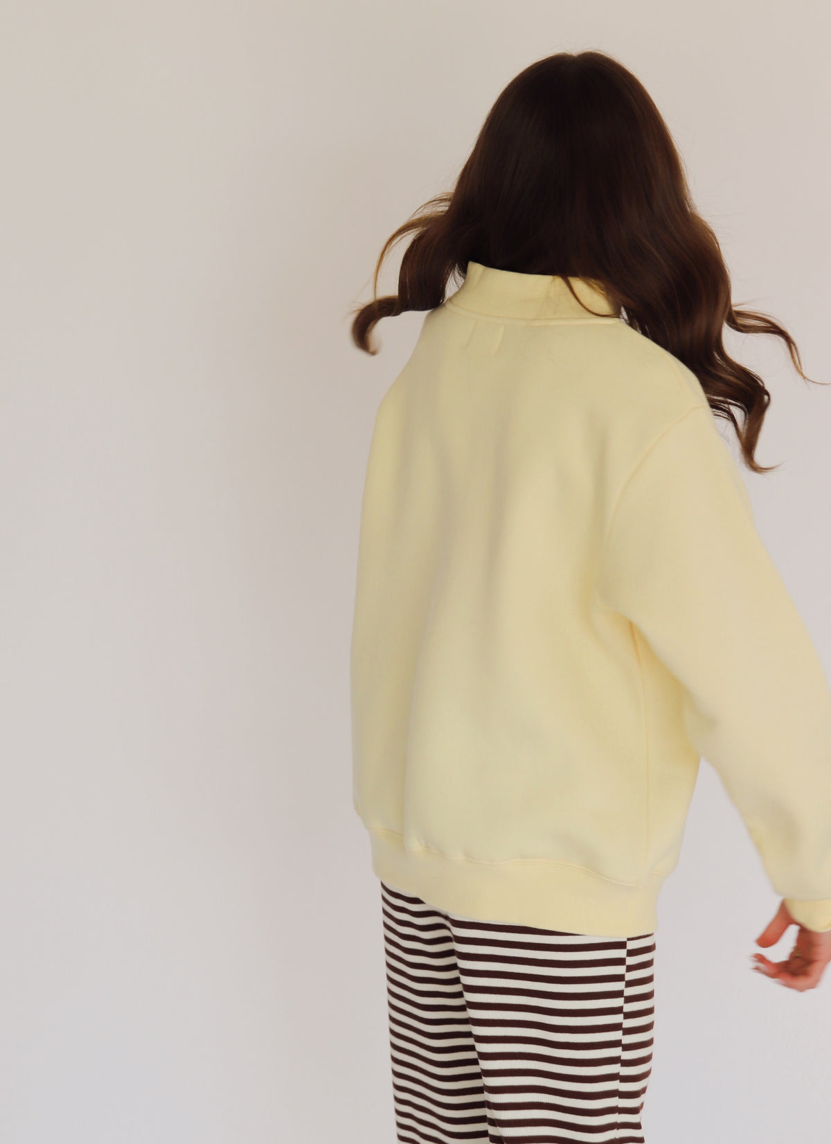Woman wearing a light yellow pullover and striped pants against a plain background