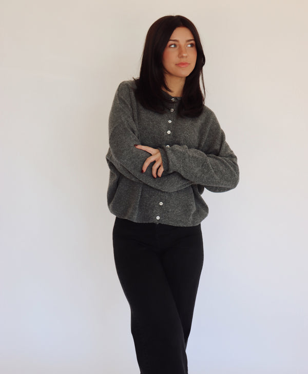 Woman wearing a gray sweater cardigan with button details against a white background