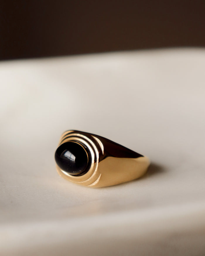 Gold ring with a black gemstone on a beige surface