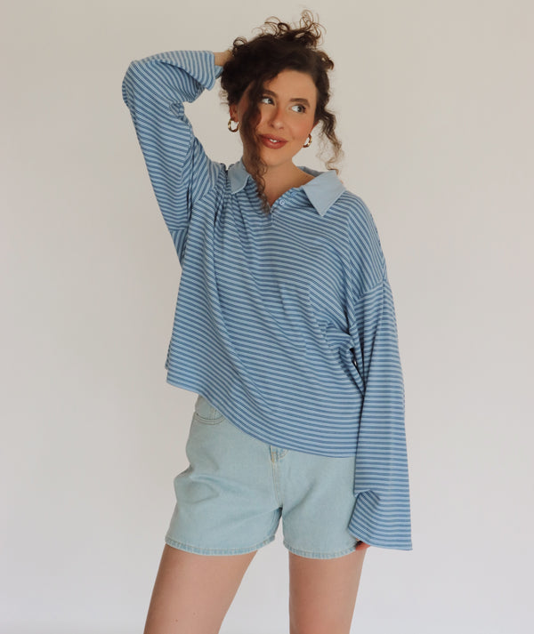 Woman wearing a blue striped shirt and light denim shorts against a plain background