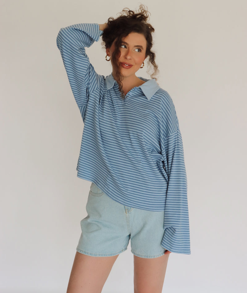 Woman wearing a blue striped shirt and light denim shorts against a plain background