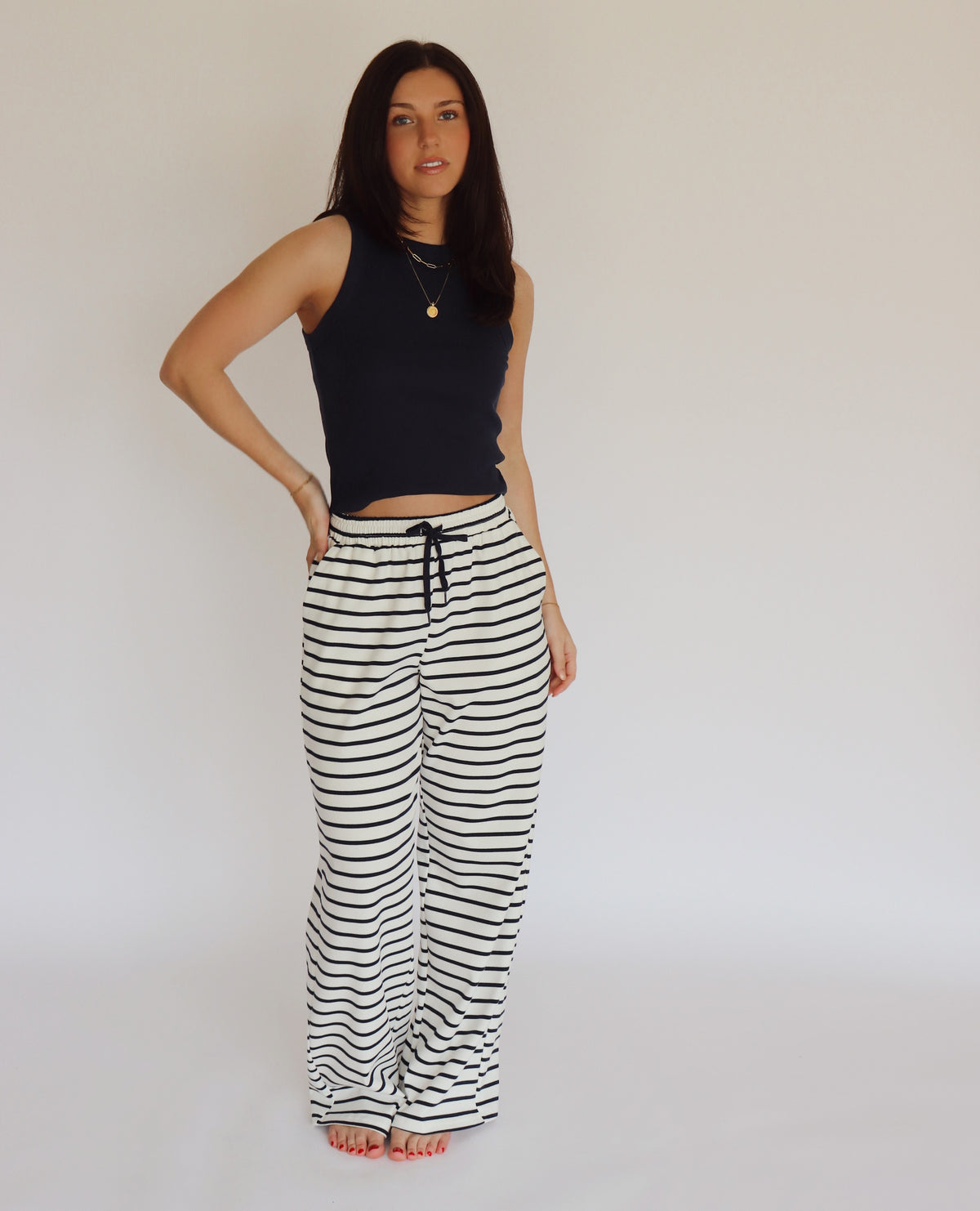 Woman wearing a navy blue sleeveless top and striped pants against a plain background