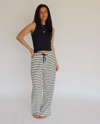 Woman wearing a navy blue sleeveless top and striped pants against a plain background