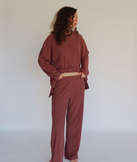 A woman modeling a matching two-piece loungewear set consisting of a long-sleeve top and pants, both featuring thin horizontal stripes in a pink and dark brown colorway.