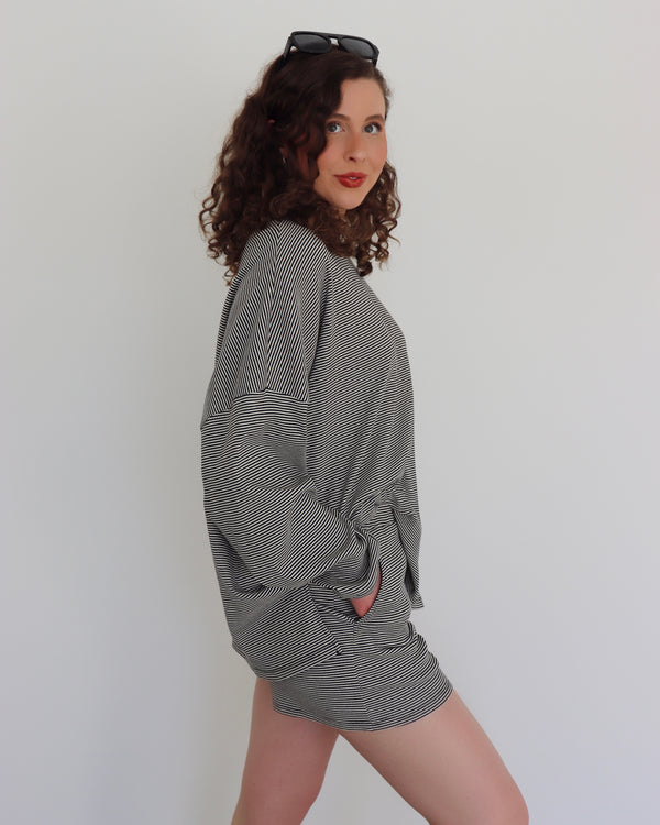 Woman wearing a black oversized top and shorts against a white background