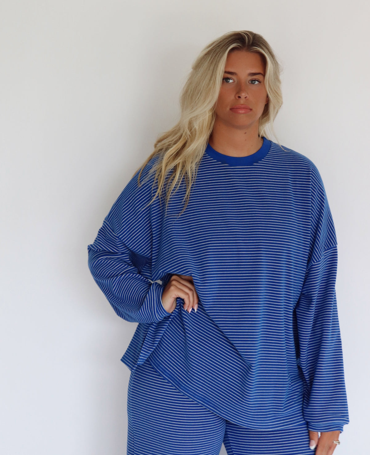 A woman modeling a matching blue striped lounge set consisting of a long-sleeve top and wide-leg pants, standing against a plain white studio background.