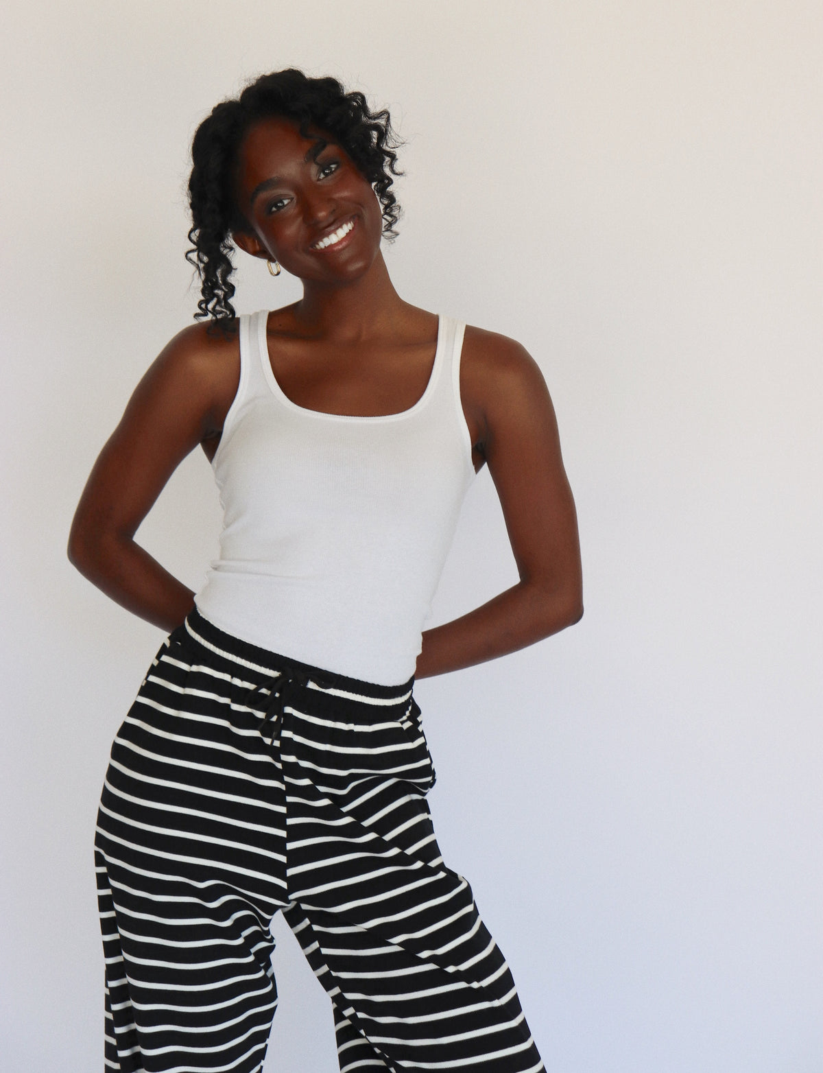Woman wearing a white tank top and black and white striped pants on a white background