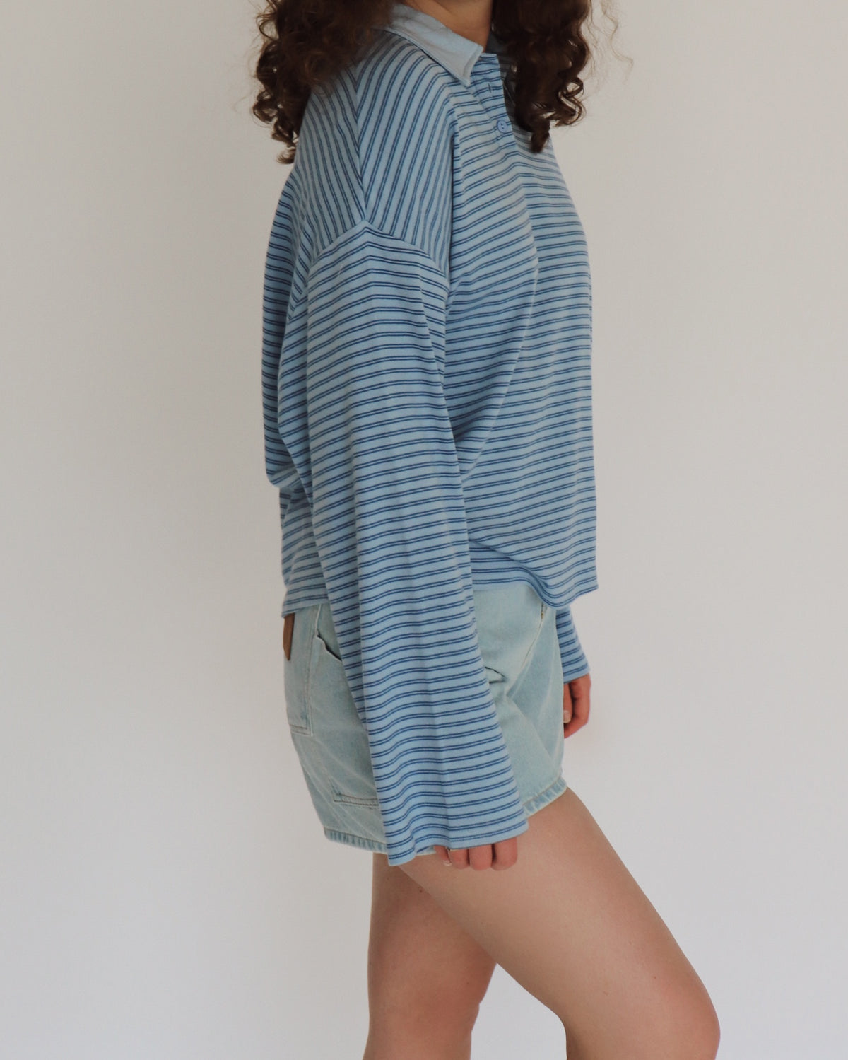 Woman wearing a blue striped shirt and light denim shorts against a plain background