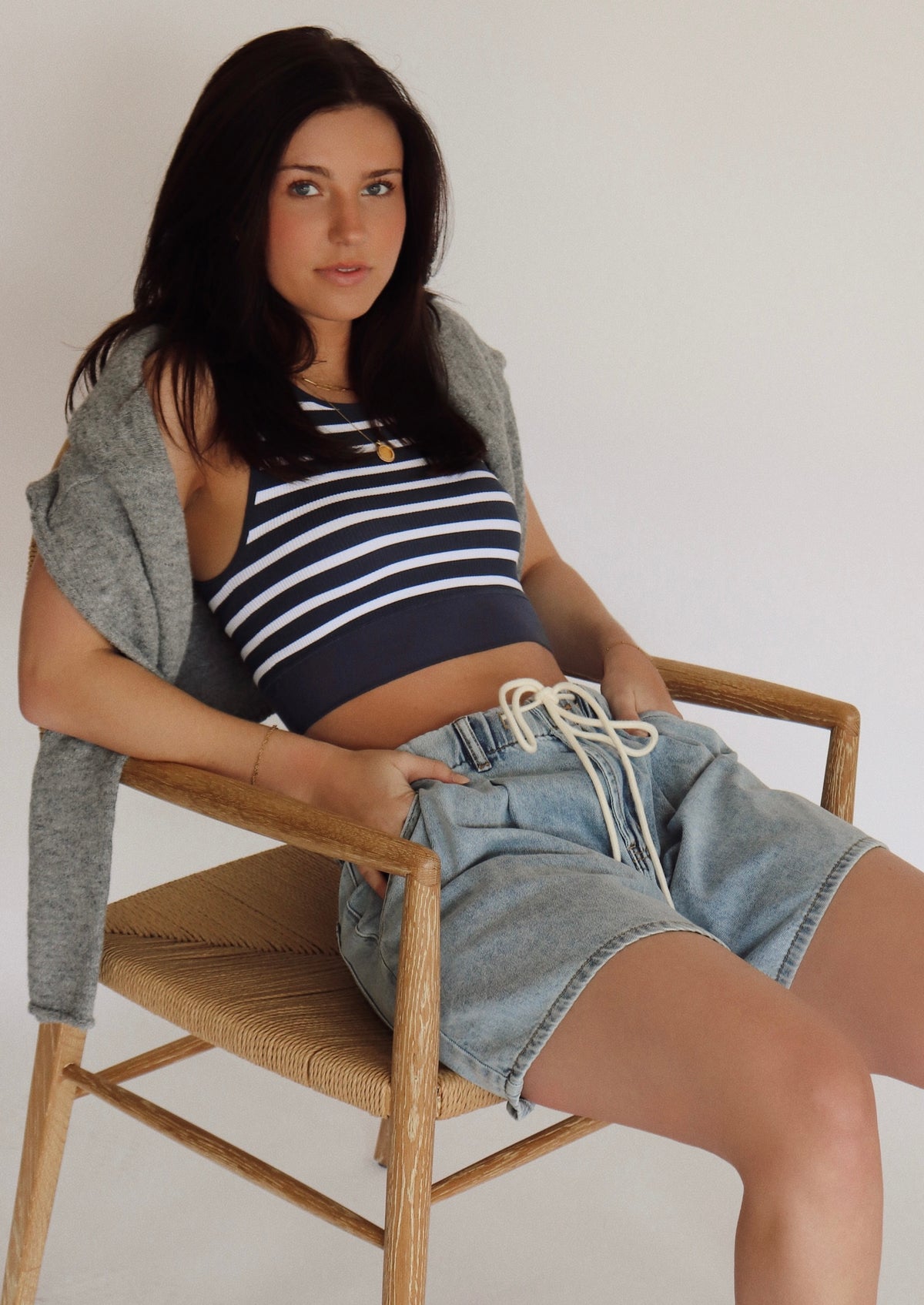 Woman sitting on a chair wearing a striped top and denim shorts.