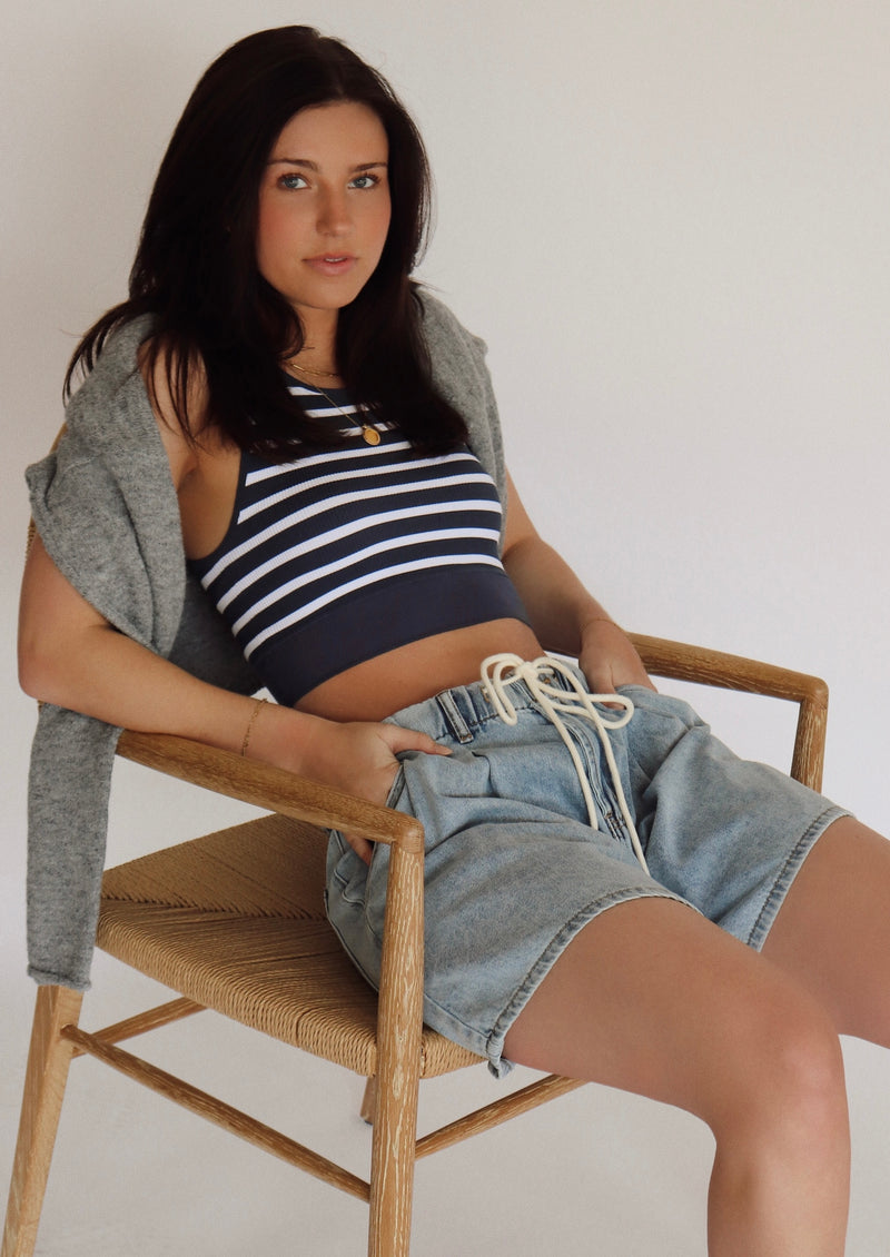 Woman sitting on a chair wearing a striped top and denim shorts.