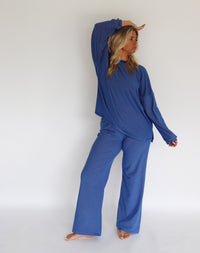 A woman modeling a matching blue striped lounge set consisting of a long-sleeve top and wide-leg pants, standing against a plain white studio background