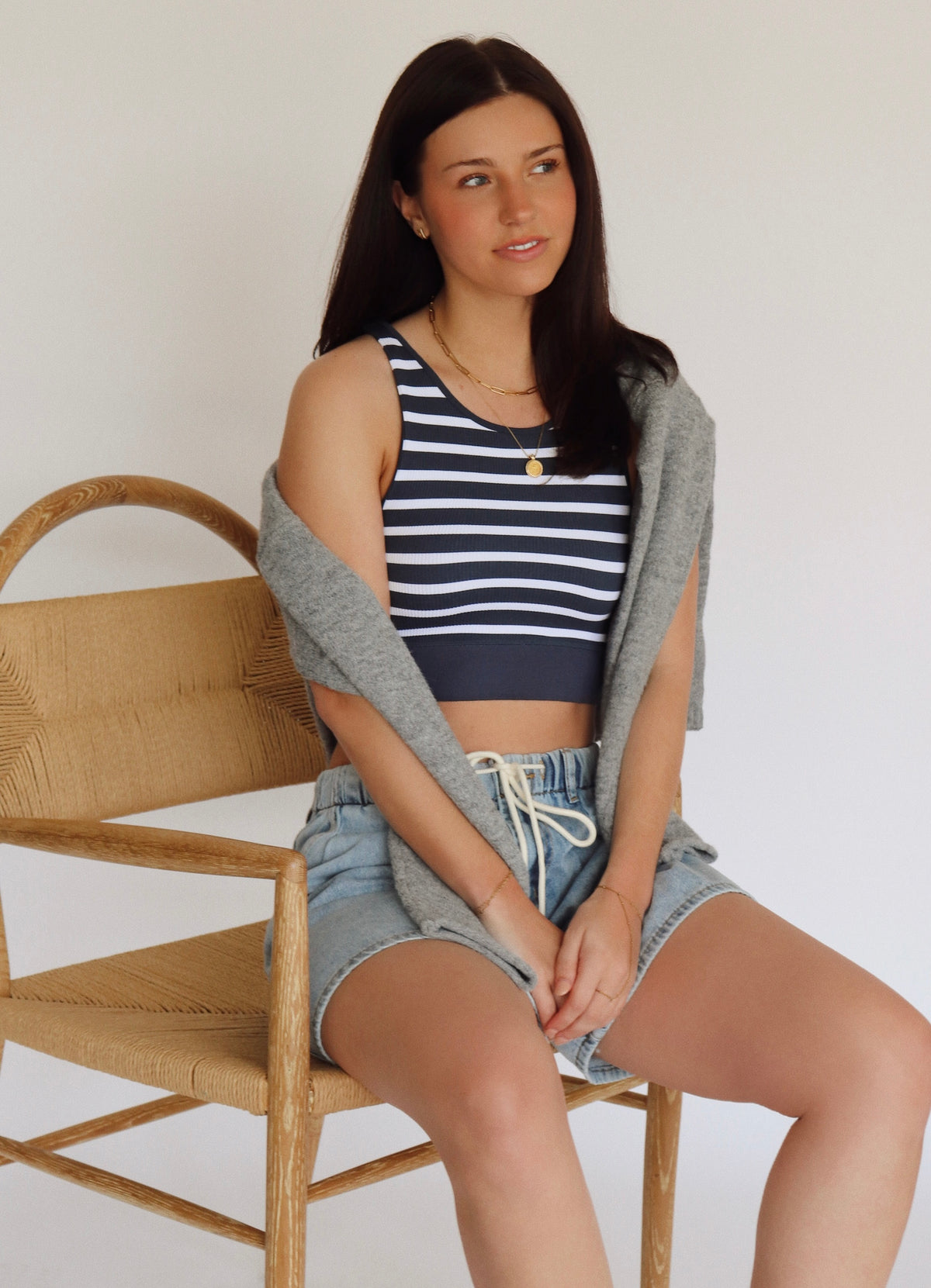 Woman sitting on a wooden chair wearing a striped tank top and shorts.