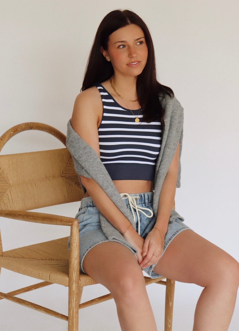 Woman sitting on a wooden chair wearing a striped tank top and shorts.
