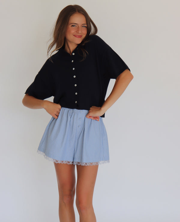 Woman wearing a navy short sleeve cardigan and light blue shorts against a white background
