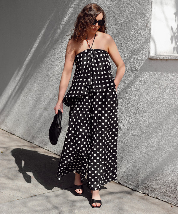 Woman in a black polka dot set standing against a gray wall.