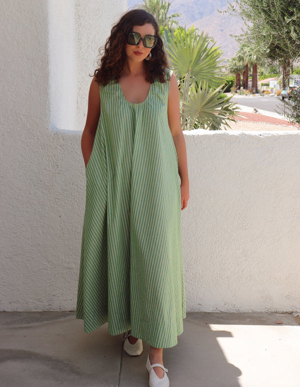 Woman wearing a green striped dress standing against a white wall with plants in the background.