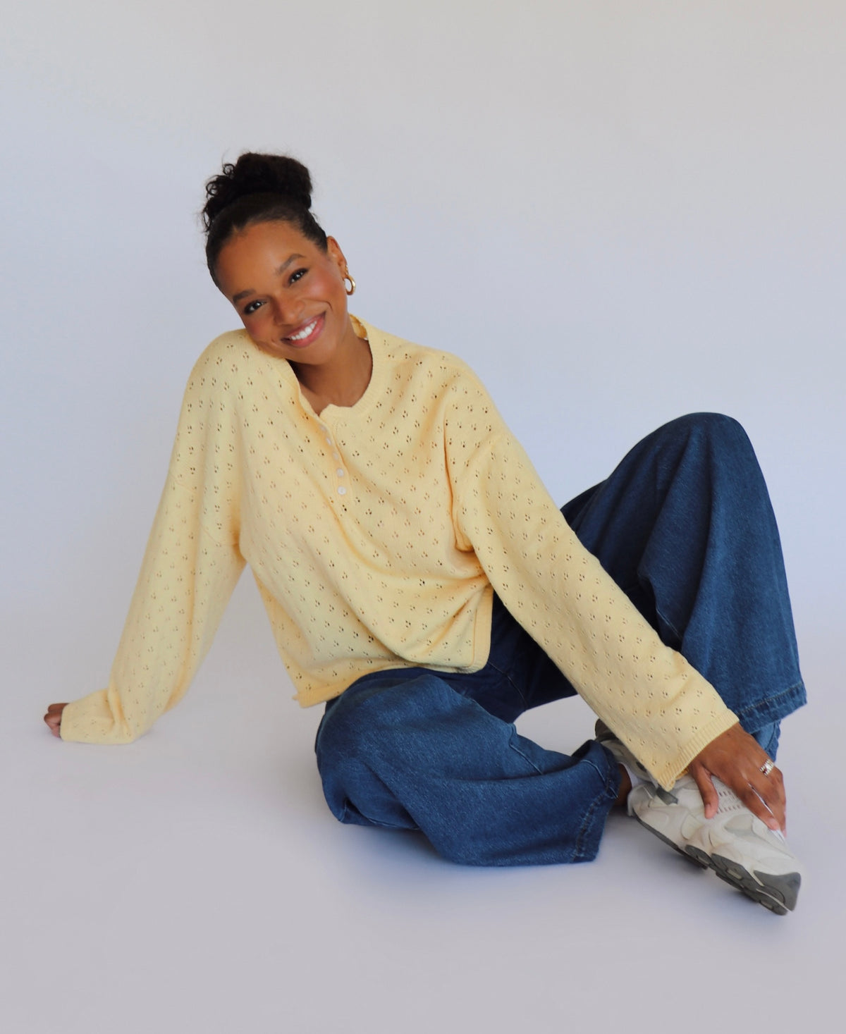 Woman wearing a yellow sweater and blue jeans sitting on a white floor.