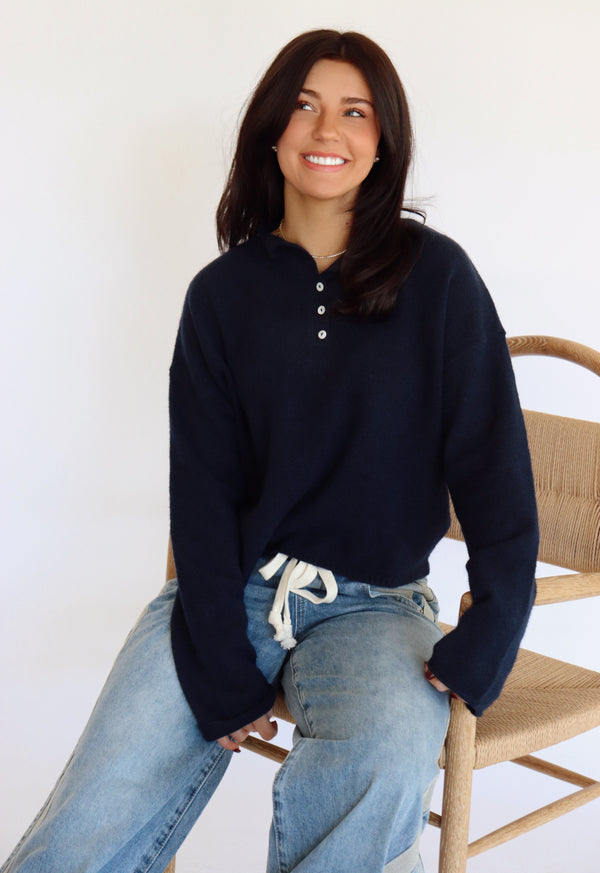 Woman wearing a navy blue sweater and jeans sitting on a wooden chair.
