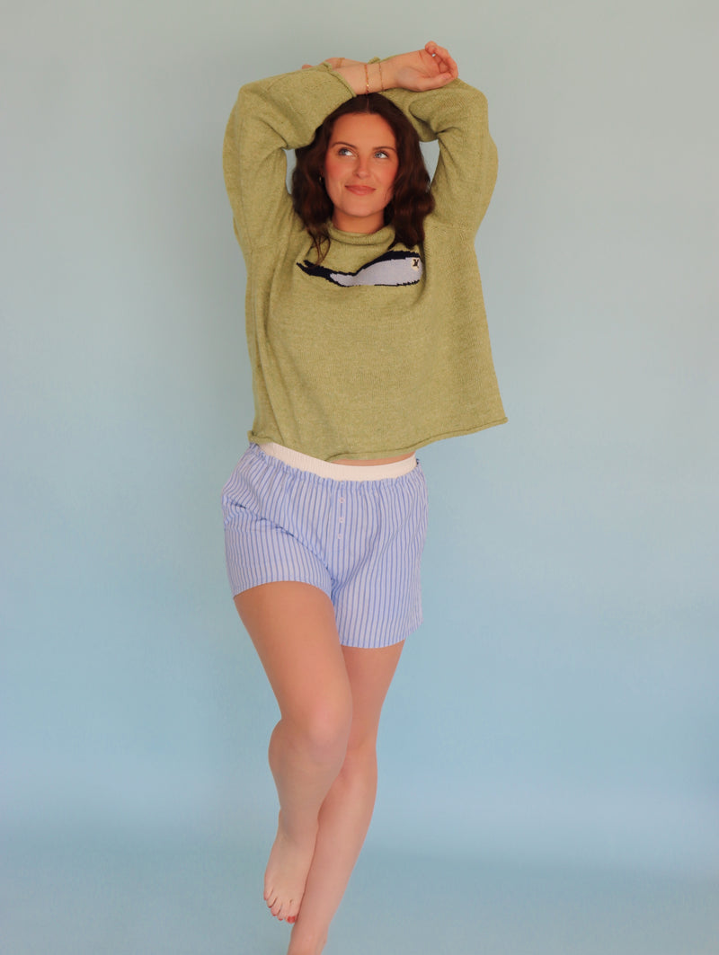 Person wearing a green sweater and striped shorts against a light blue background