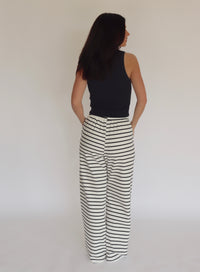Woman wearing a dark navy blue tank top and striped pants against a plain background