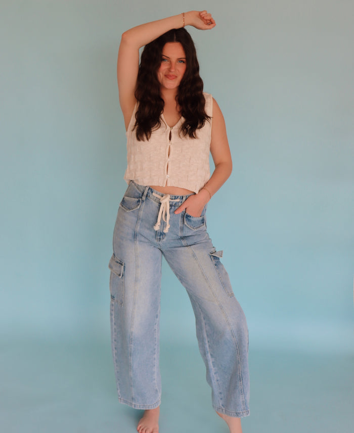 Woman wearing a vest and jeans against a plain background