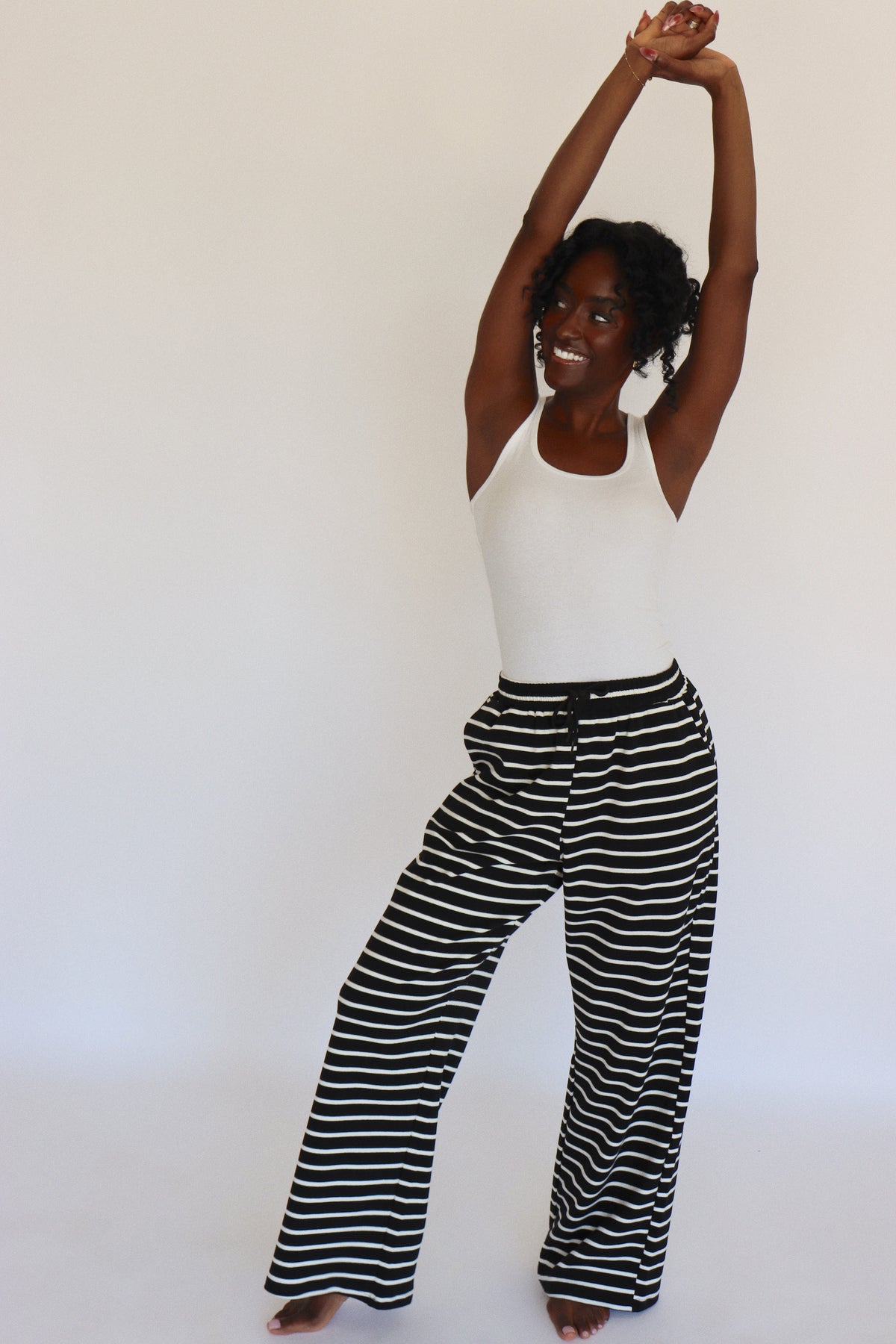 Woman wearing a white tank top and black and white striped pants on a white background