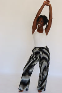 Woman wearing a white tank top and black and white striped pants on a white background