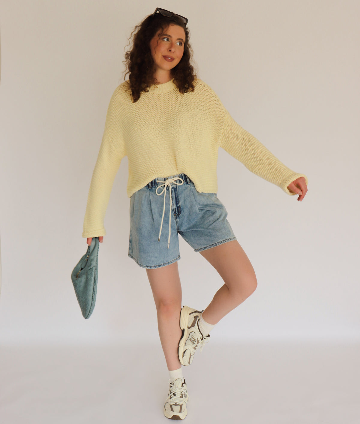 Person wearing a yellow sweater and denim shorts against a plain background