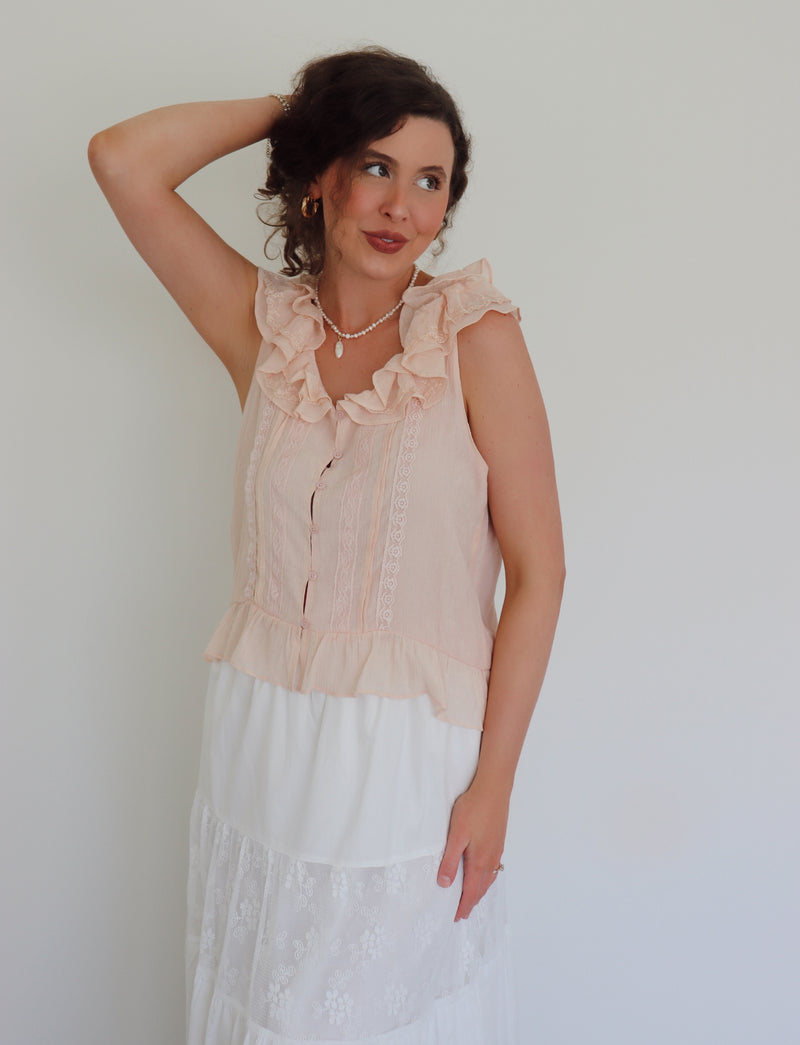 Woman wearing a light pink blouse with ruffled neckline against a plain background