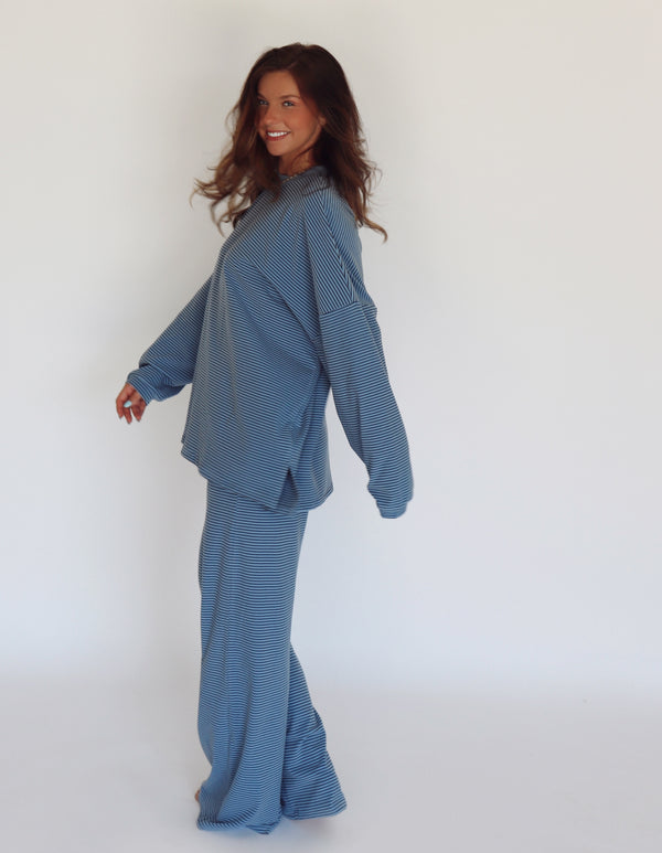 A woman modeling a matching blue striped lounge set, consisting of a long-sleeve top and wide-leg pants, against a plain white studio background.