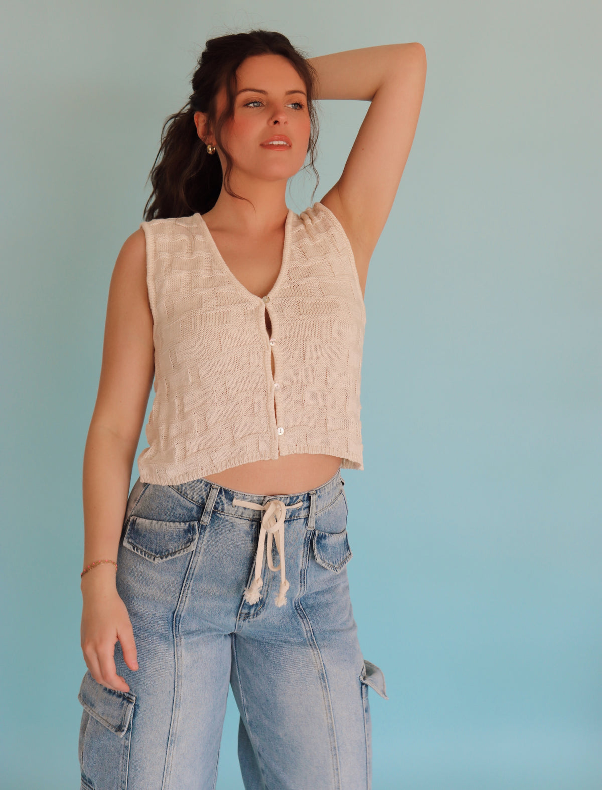Woman wearing a cream vest and blue jeans against a light blue background