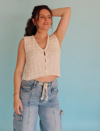 Woman wearing a cream vest and blue jeans against a light blue background