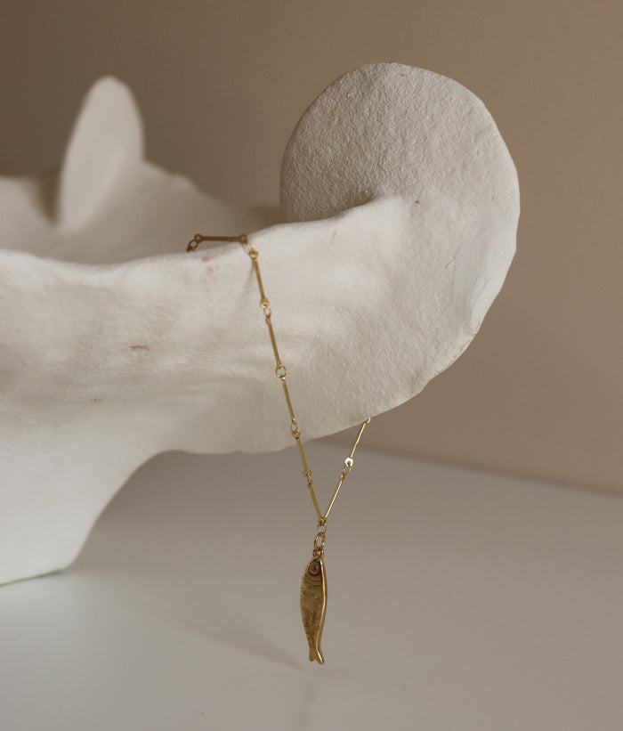 Gold necklace with a fish pendant on a neutral background