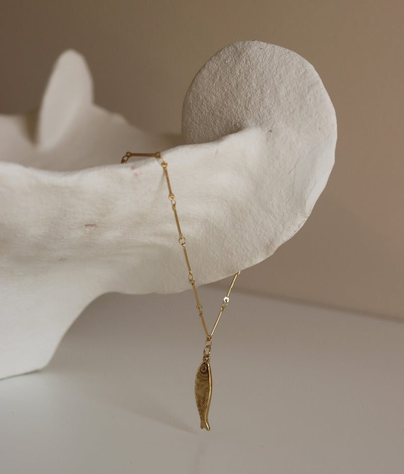 Gold necklace with a fish pendant on a neutral background