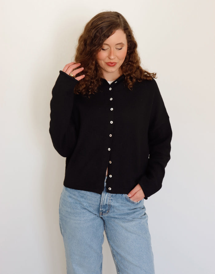 Person wearing a black cardigan and light blue jeans against a white background