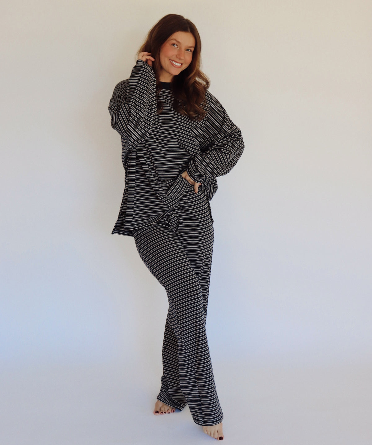 A woman modeling a matching two-piece loungewear set consisting of a long-sleeve top and wide-leg pants, both featuring a navy and white horizontal stripe pattern, set against a plain white studio background.