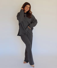 A woman modeling a matching two-piece loungewear set consisting of a long-sleeve top and wide-leg pants, both featuring a navy and white horizontal stripe pattern, set against a plain white studio background.