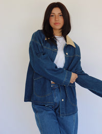 Person wearing a blue denim jacket and denim pants against a white background
