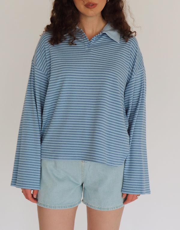 Woman wearing a blue striped shirt and light denim shorts against a plain background