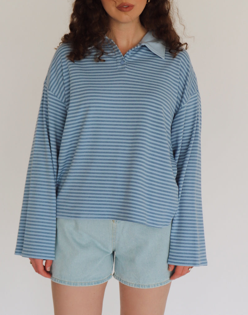 Woman wearing a blue striped shirt and light denim shorts against a plain background