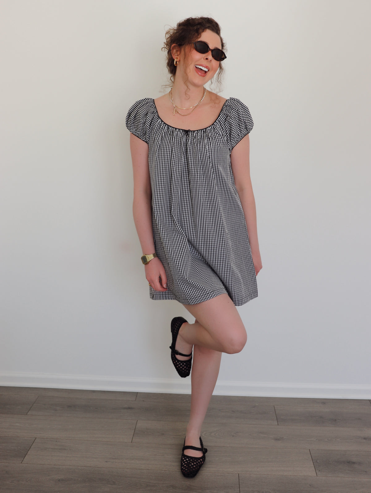 Woman wearing a black and white checkered dress against a white wall.