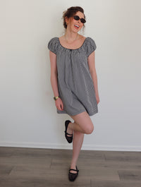 Woman wearing a black and white checkered dress against a white wall.