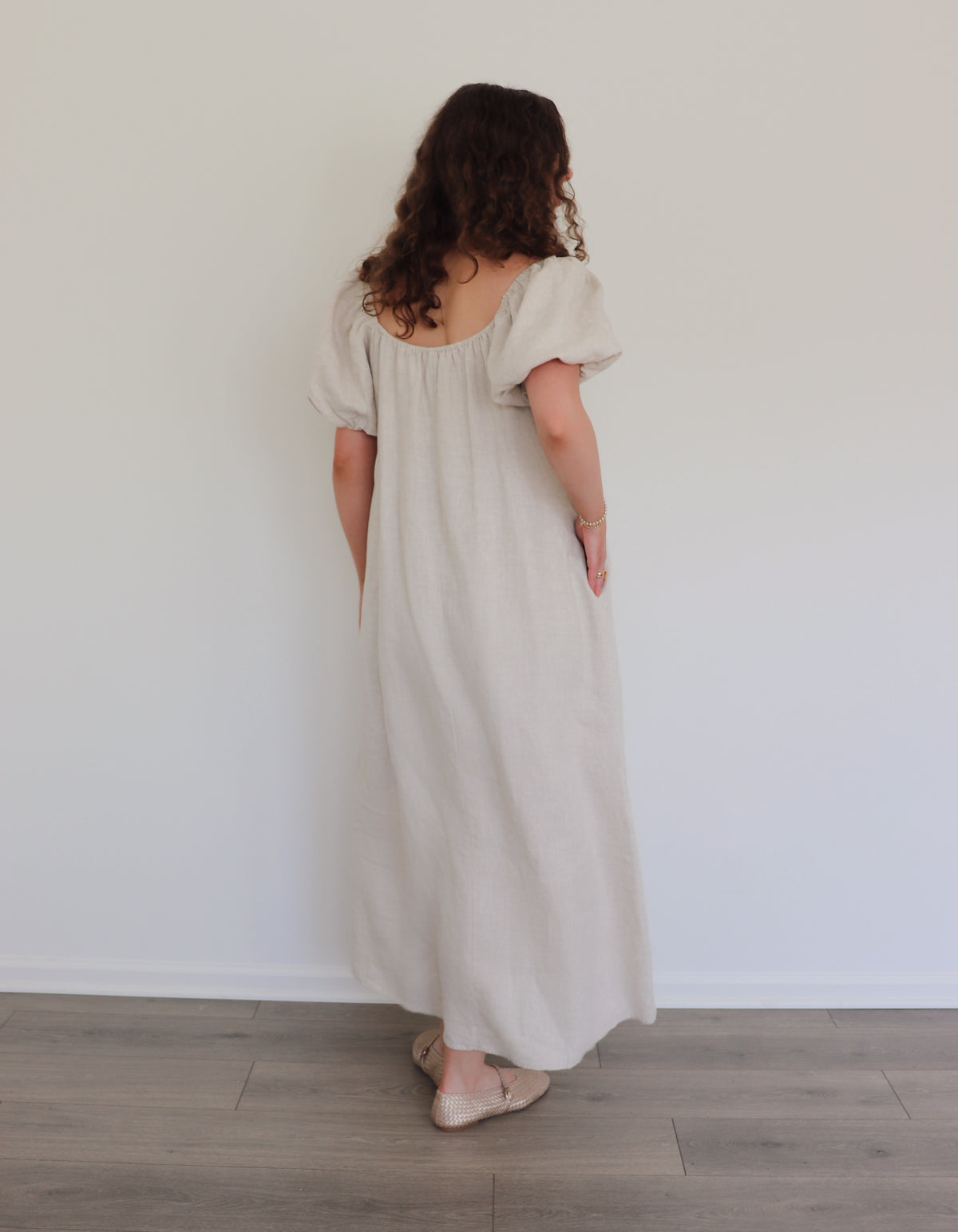 Woman wearing a long beige linen dress against a white wall