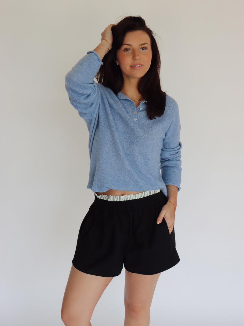 Woman wearing a blue long-sleeve shirt and dark navy shorts against a white background