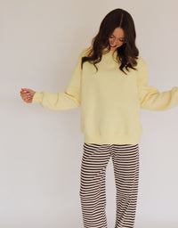 Woman wearing a light yellow pullover and striped pants against a plain background