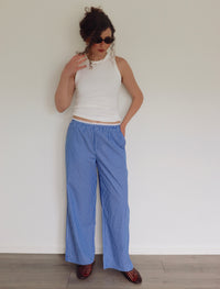 Woman wearing a white sleeveless top and blue striped pants against a plain background
